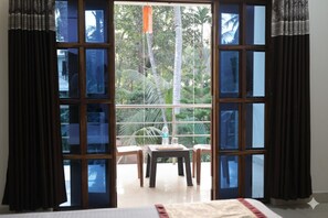A room with a large sliding glass door leading to a balcony with a table and chairs. - Sidhivinayak Resort Devbag Sangam Beach  (Malvan)