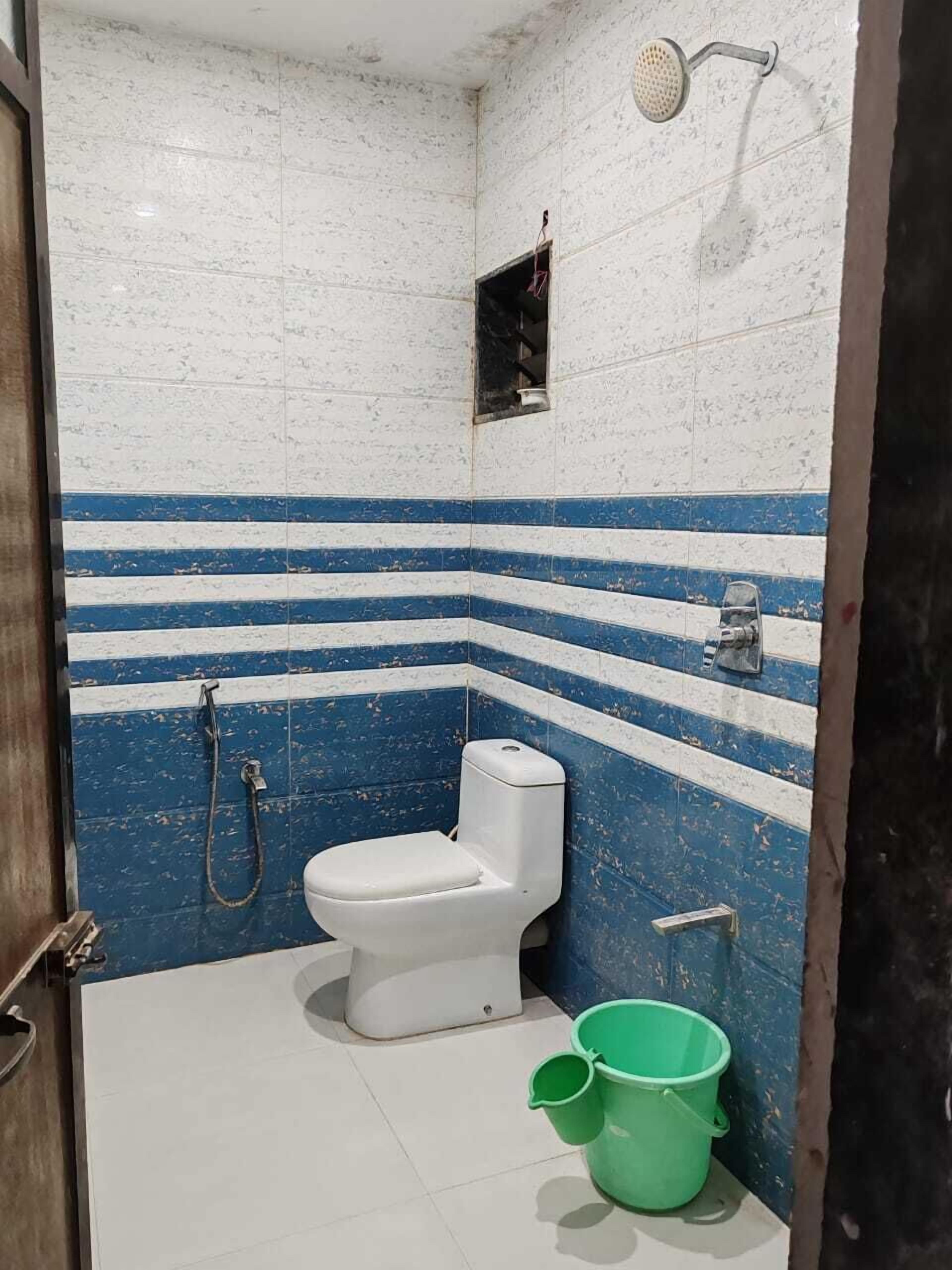 A small bathroom with a toilet, a shower, and a green bucket on the floor.