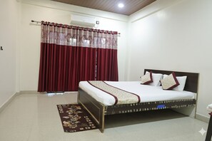 A bedroom with a bed, curtains, an air conditioning unit, and a decorative rug. - Sidhivinayak Resort Devbag Sangam Beach  (Malvan)