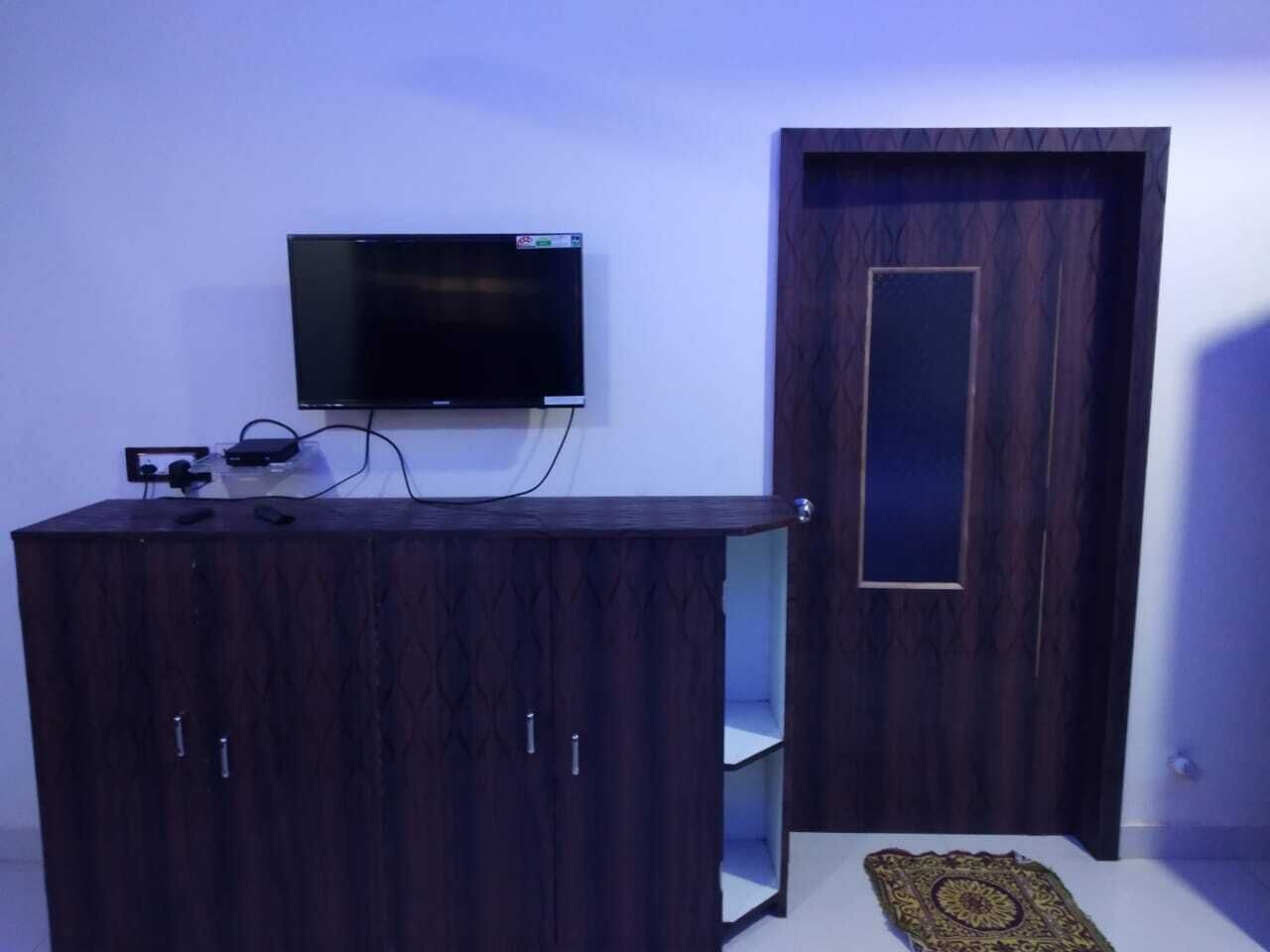 A room with a dark wooden cabinet, a flat-screen TV mounted on the wall, and a door with a vertical panel.