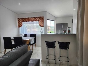 Una cocina moderna con zona de comedor, que incluye una barra, dos taburetes, un sofá y una mesa con sillas.