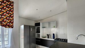 A modern kitchen with a stainless steel refrigerator, black cabinets, a marble-tiled floor, and a black countertop. - Perequê-Açú - 200m from the beach • Air conditioning • Grill • 8 Guests (Perequê-Acu Ubatuba)