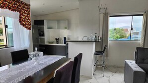 A modern kitchen with a dining area, a bar stool, and a view of the city through large windows. - Perequê-Açú - 200m from the beach • Air conditioning • Grill • 8 Guests (Perequê-Acu Ubatuba)