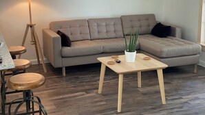 Un salon moderne avec un canapé d’angle gris, une petite table basse en bois, un lampadaire et une plante en pot.
