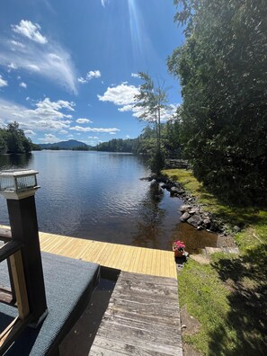 A wooden dock leading to a calm lake with a clear sky and mountains in the distance.