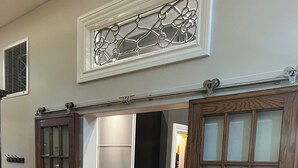 A hallway with a wooden floor, a sliding door, and a white wall with a decorative window.