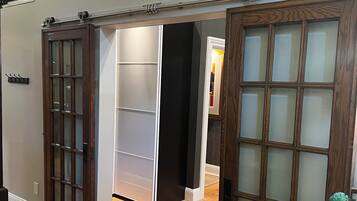 Un couloir doté d’un plancher en bois, d’une porte coulissante et d’un mur blanc orné d’une fenêtre décorative.
