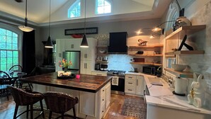 A modern kitchen with a central island, wooden chairs, a dining table, and a large window.