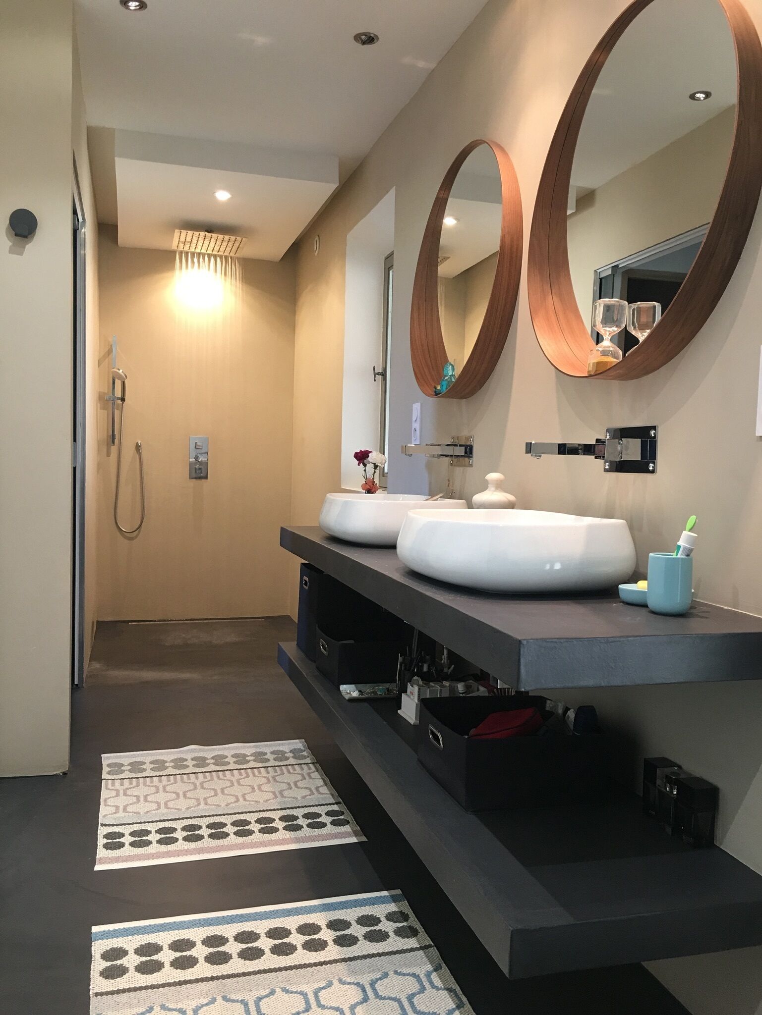 Une salle de bain moderne avec un grand miroir, deux lavabos, une douche et un tapis à motifs.