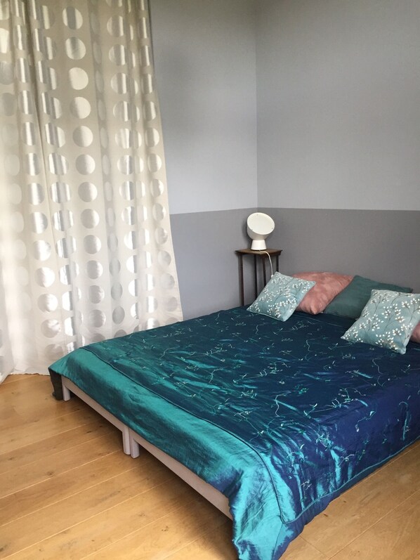 A bedroom with a teal bedspread, a round bedside table, and a pillow with a floral pattern.