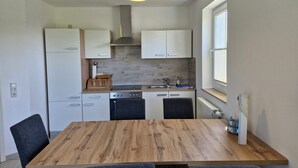 A modern kitchen with white cabinets, a wooden dining table, and a hanging light fixture.