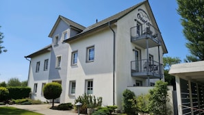 A two-story building with a balcony on the upper floor, a paved driveway, and a well-maintained garden.