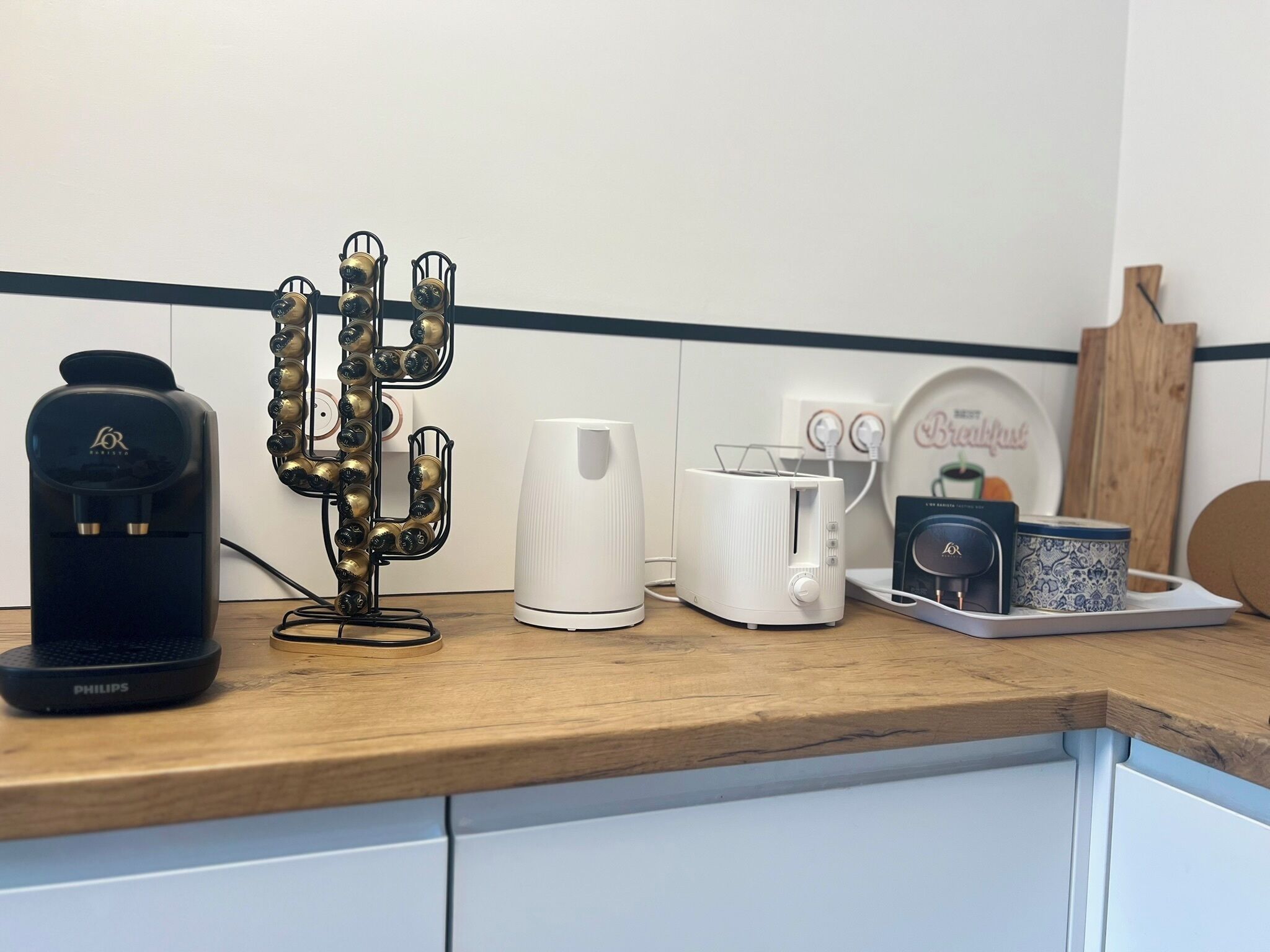 A kitchen counter with a coffee maker, a white kettle, a toaster, and a decorative metal stand.