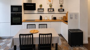 A modern kitchen with built-in appliances, a dining table with chairs, and decorative items on shelves.