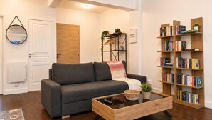 A modern living room with a grey sofa, a wooden coffee table, a bookshelf, and a door.