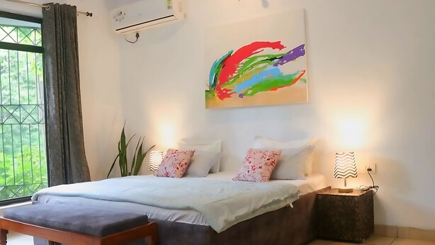 A bedroom with a bed, bedside lamps, a painting, and a view through a window.