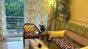 A living room with a sofa, a bench, and a chair, a potted plant, and a view of greenery outside.