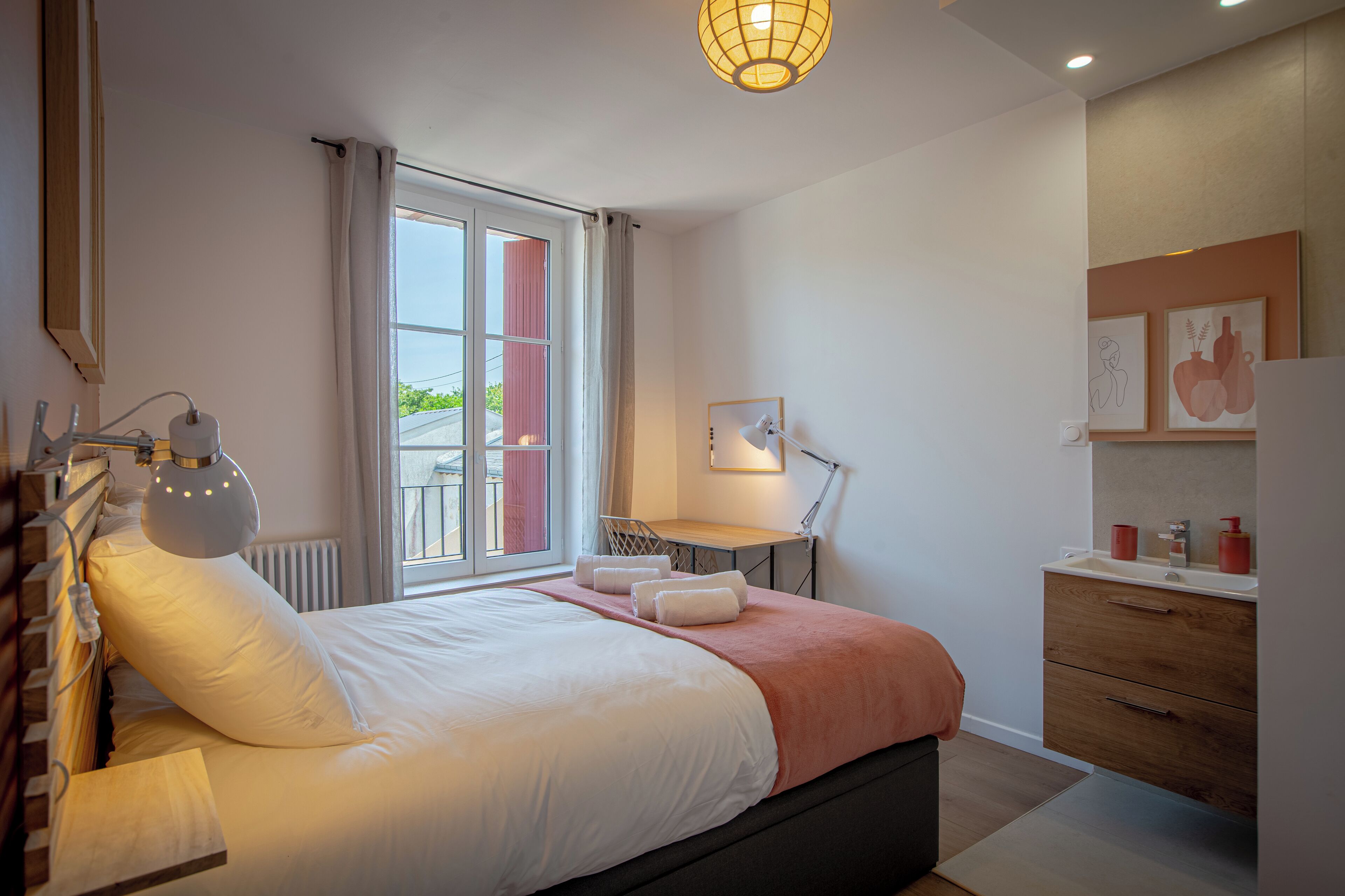 Une chambre à coucher moderne avec un lit, une table de chevet, une lampe et une vue sur l’extérieur.