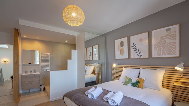 Une chambre d’hôtel moderne avec un grand lit, une table de chevet, un miroir et des œuvres d’art accrochées au mur.