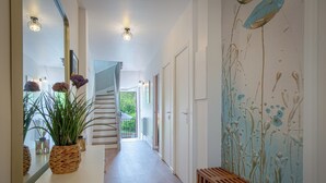 Un couloir avec un banc en bois, un pot de fleurs en osier et un mur orné d’un motif abstrait bleu et blanc.