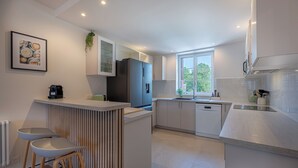 Une cuisine moderne avec des meubles blancs, un îlot central intégré doté de tabourets, un réfrigérateur et une fenêtre laissant entrer la lumière naturelle.