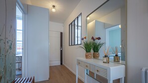 Un couloir avec une console blanche, un miroir et une porte donnant sur une autre pièce.