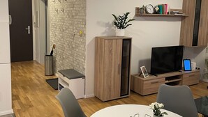 A modern living room with a white round table, grey chairs, a TV, and a bookshelf.