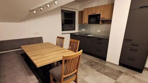 A compact kitchen with a dining area, including a wooden table and chairs, a bench, and a built-in oven. - Almhaus Hochenwarter Apartment 4 (Kärnten)