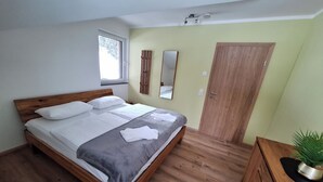 A bedroom with a wooden bed, a window, a mirror, a door, and a plant. - Almhaus Hochenwarter Apartment 4 (Kärnten)