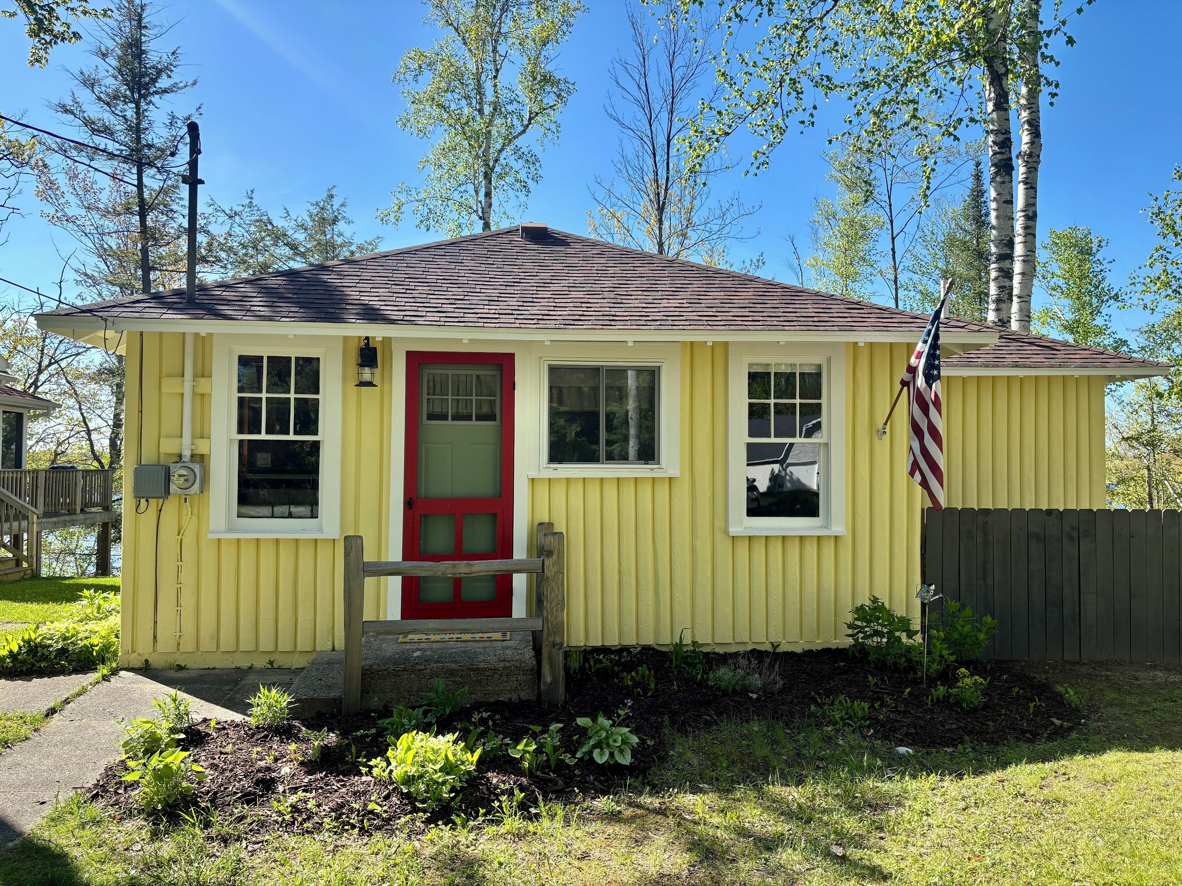 A yellow house with a red door, a small porch, and an American flag.