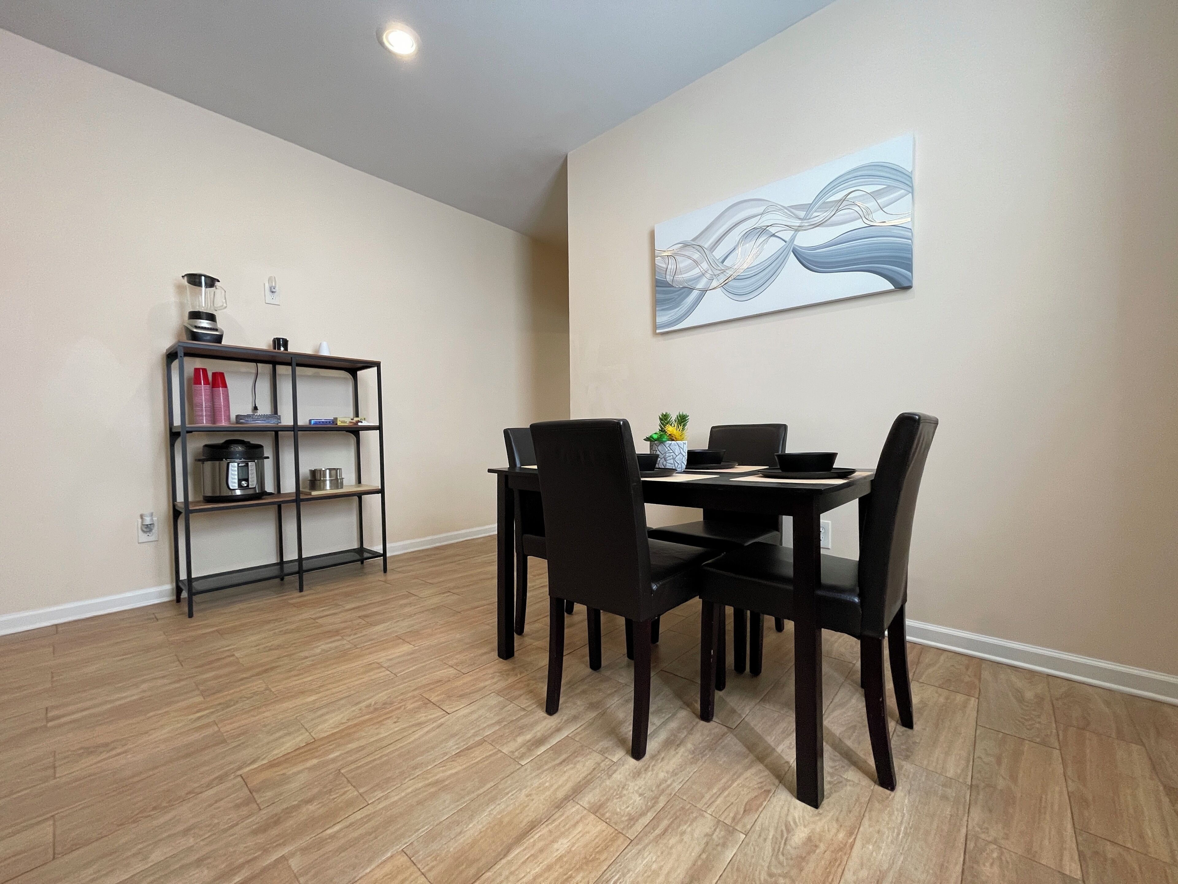 Un comedor con una mesa, sillas, una estantería y un cuadro en la pared.