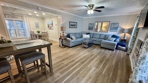 A spacious living area with a wooden floor, a dining table with benches, a sofa set, and a ceiling fan. - Pet-Friendly Ocean Lakes 4BR | 2 Golf Carts | Sleeps 10 | Large Lot (Myrtle Beach)