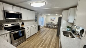 A modern kitchen with white cabinets, stainless steel appliances, and a wooden floor. - Pet-Friendly Ocean Lakes 4BR | 2 Golf Carts | Sleeps 10 | Large Lot (Myrtle Beach)