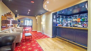 A hotel lobby with a bar area, sofas, and a red carpeted floor.
