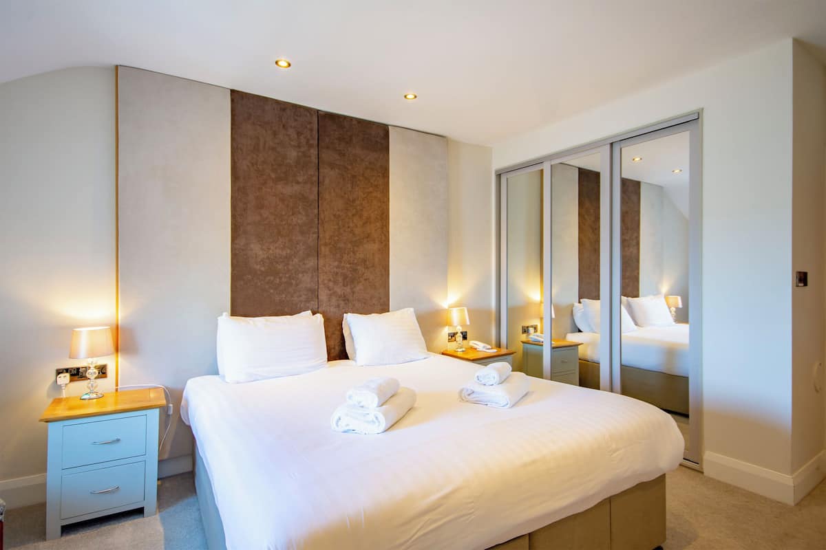 A modern hotel room with a large bed, bedside tables, a wardrobe, and a mirror.