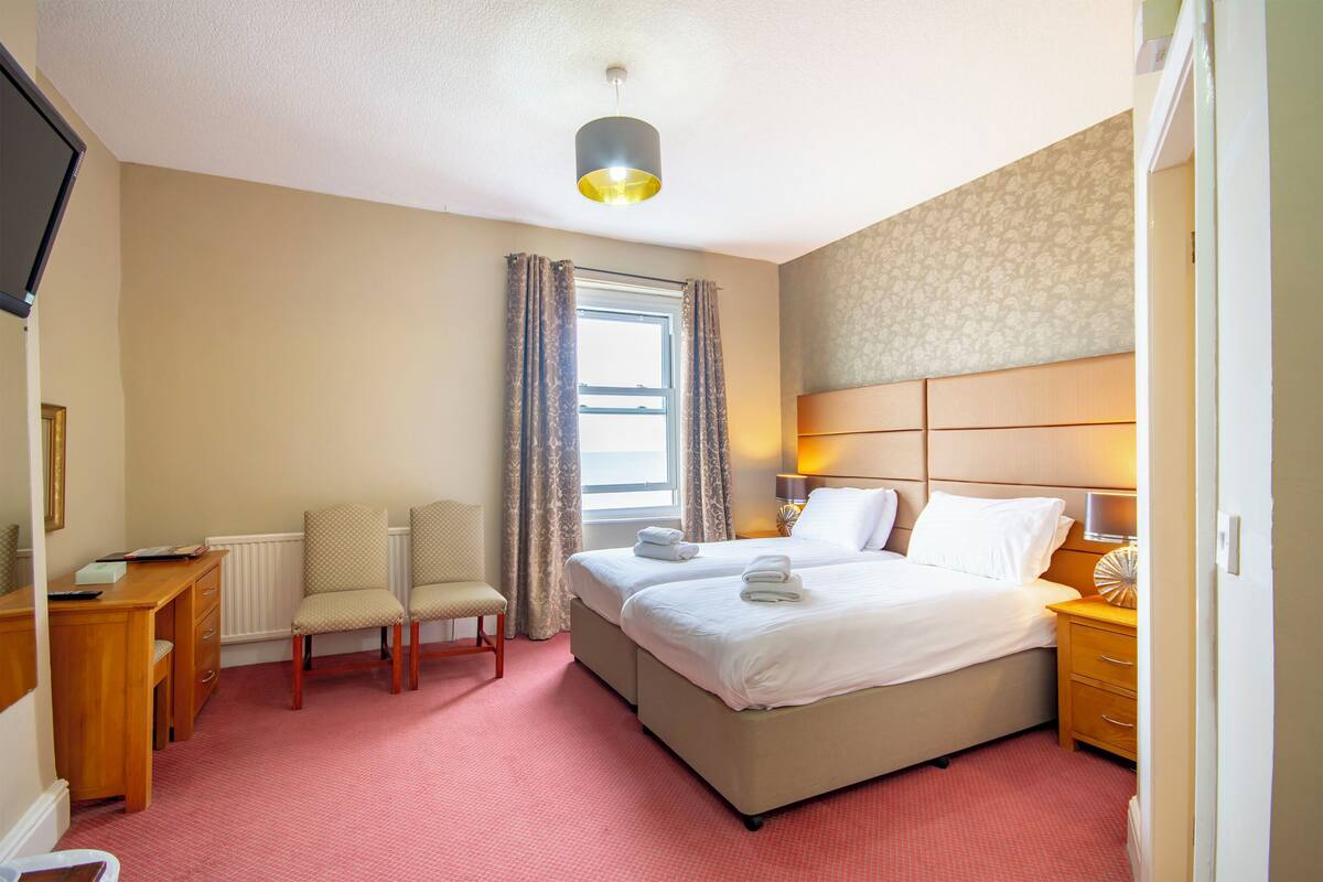 A hotel room with a bed, two chairs, a desk, a lamp, and a television.