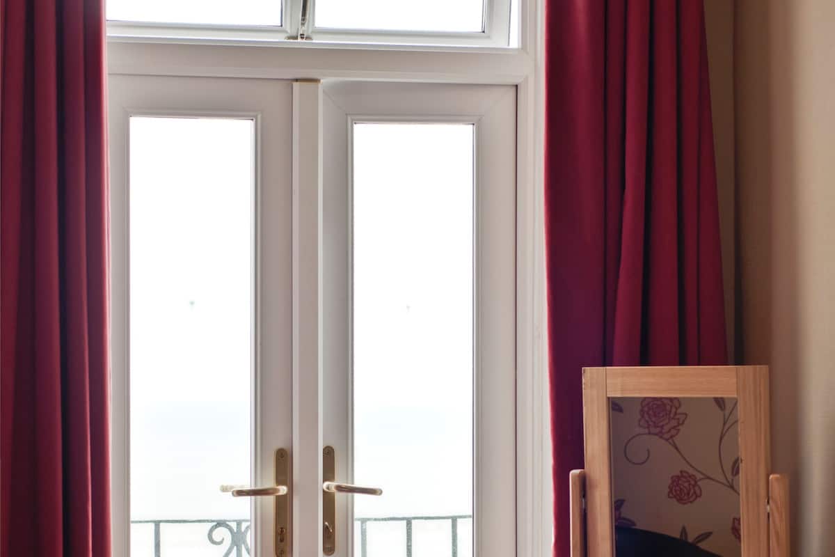 A room with a bed, a desk with a mirror, and a view through a door.