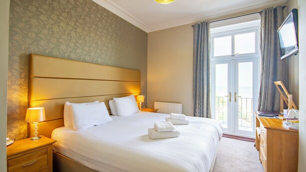 A hotel room with a large bed, bedside tables, a desk, a television, and a view of the outdoors.