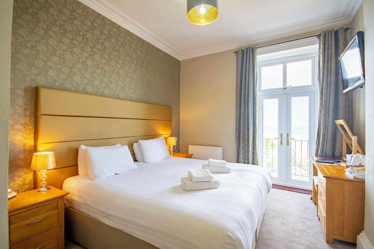 A hotel room with a large bed, bedside tables, a desk, a television, and a view of the outdoors.