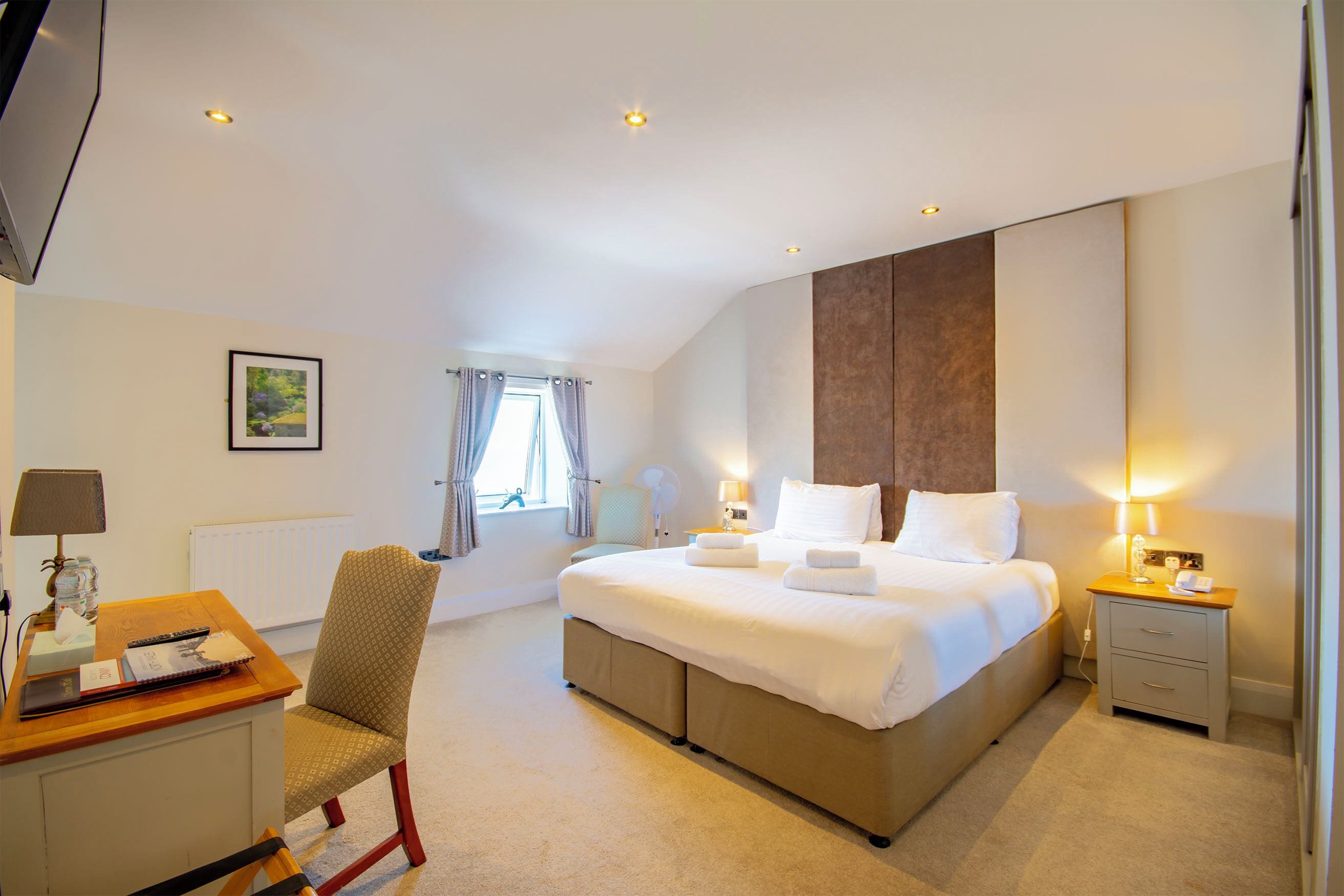 Een hotelkamer met een bed, nachtkastje, stoel, bureau, lamp en een raam met gordijnen.