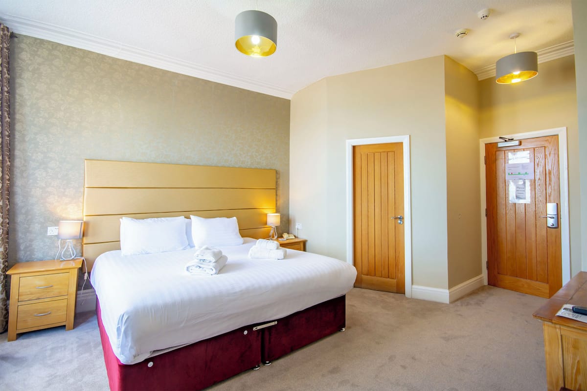 A hotel room with a large bed, bedside tables, a wooden door, and a carpeted floor.
