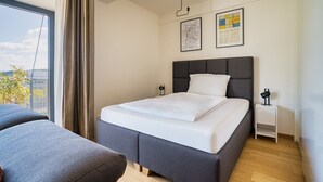 A modern hotel room with a large bed, a small bedside table, a nightstand, and a view of the outdoors.