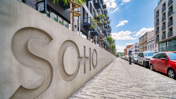 A paved pathway leading to a building with a large 'S' and 'O' sign, suggesting a hotel or similar establishment.