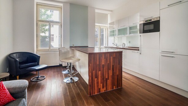 Une cuisine moderne avec des meubles blancs, un îlot central en bois, un tabouret de bar noir et une chaise bleue.
