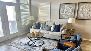 A living room with a sofa, coffee table, and two chairs. There are two lamps, a rug, and artwork on the wall. - Homey lakefront condo on quiet cove in Hot Springs (Hot Springs)