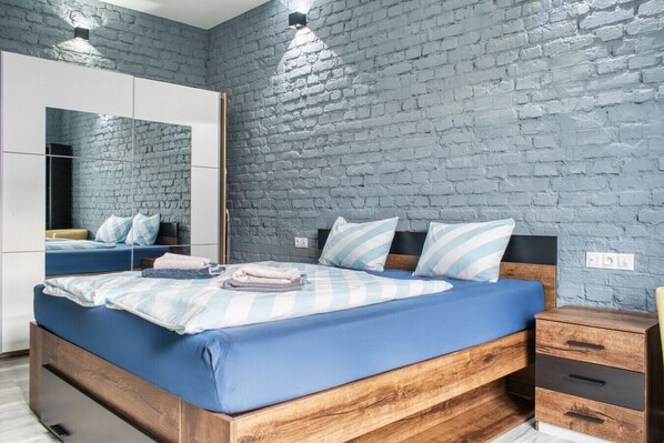 A modern bedroom with a brick wall, a large mirror, a wooden bed frame, and a nightstand with drawers. - Karlovy Cute Inn: 1BR apartment w/ Elegant bath (Karlovy Vary)