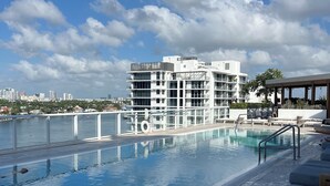 A rooftop pool with clear blue water, lounge chairs, and a modern building in the background. - 5-Star Luxury Condo at Tiffany House, two rooftop pools, one block from beach (Fort Lauderdale)
