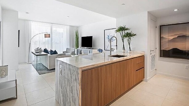 A modern kitchen with a marble island, wooden cabinets, and a built-in sink. - 5-Star Luxury Condo at Tiffany House, two rooftop pools, one block from beach (Fort Lauderdale)