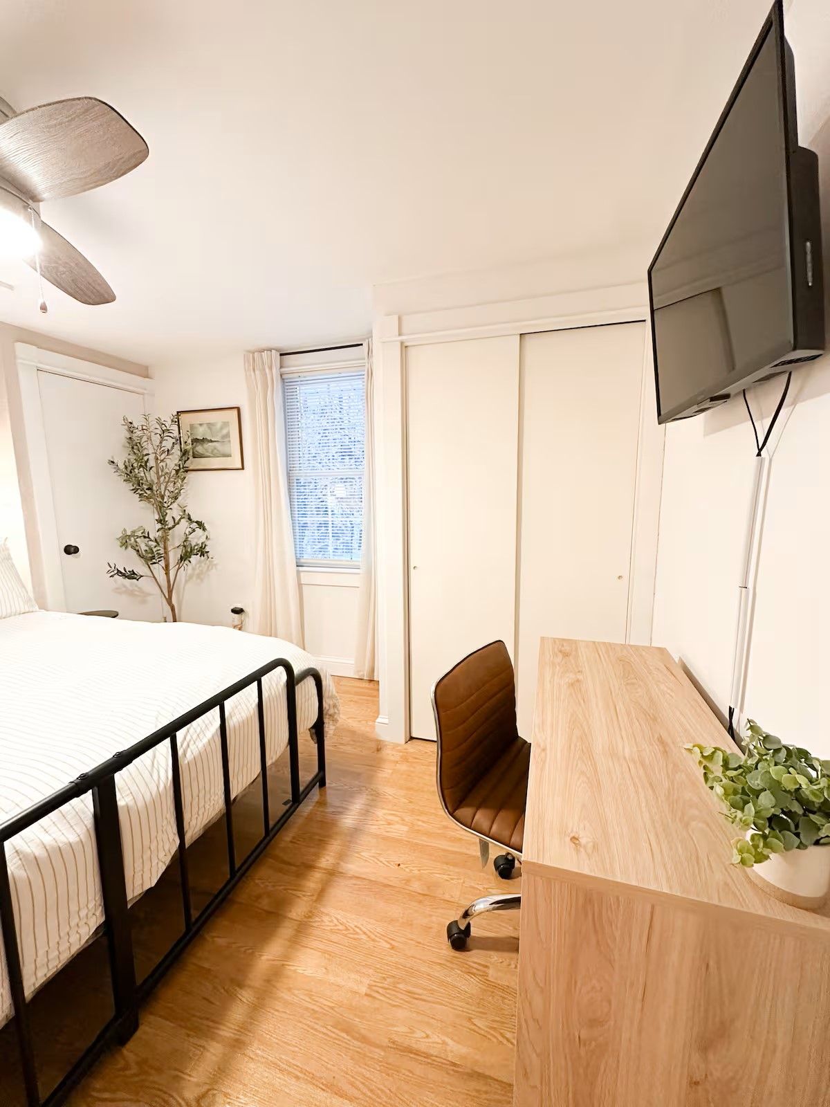 Een slaapkamer met een bed, bureau, stoel, televisie en een raam met gordijnen.