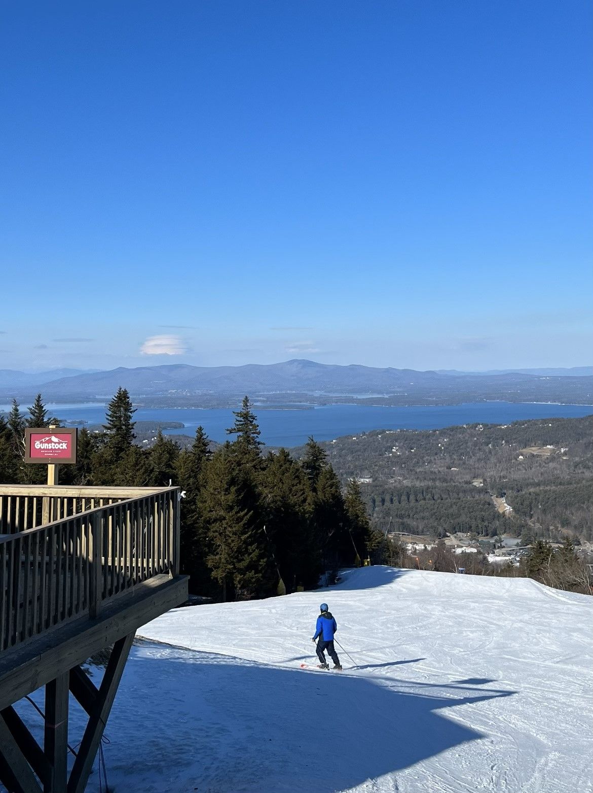 A ski slope with a clear view of a lake and mountains in the distance.